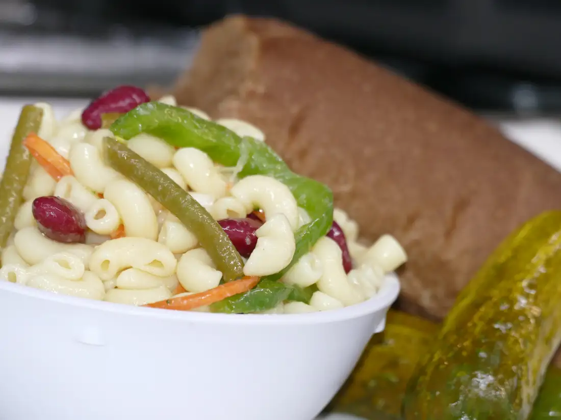 Pasta salad and a pickle on a plate with a sandwich. 