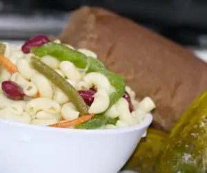 Pasta salad and a pickle on a plate with a sandwich. 